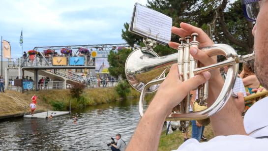 Trompetspeler speelt en kijkt in de richting van het kanaal en de voetgangersbrug in Adinkerke.
